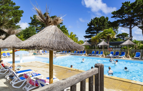 Piscina all'aperto al Flower Camping Port de la Chaîne in Bretagna, Francia, con lettini e ombrelloni di paglia.