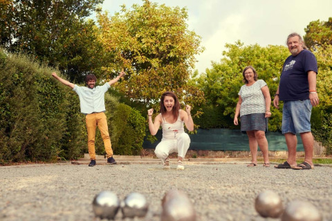 Vier mensen spelen jeu de boules op een grindbaan omringd door groen bij Flower Camping Port de la Chaîne.