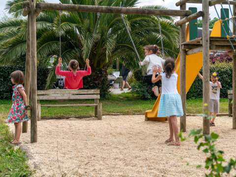 Des enfants jouent sur une aire de jeux avec balançoires et toboggan au Flower Camping Port de la Chaîne, Bretagne.