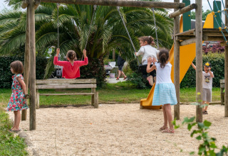 Bambini che giocano su un parco giochi con altalene e scivolo a Flower Camping Port de la Chaîne in Bretagna, Francia.