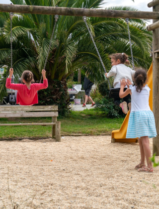 Des enfants jouent sur une aire de jeux avec balançoires et toboggan au Flower Camping Port de la Chaîne, Bretagne.