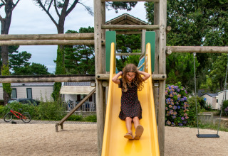 Ein Mädchen rutscht eine gelbe Rutsche auf dem Spielplatz im Flower Camping Port de la Chaîne in Bretagne hinunter.