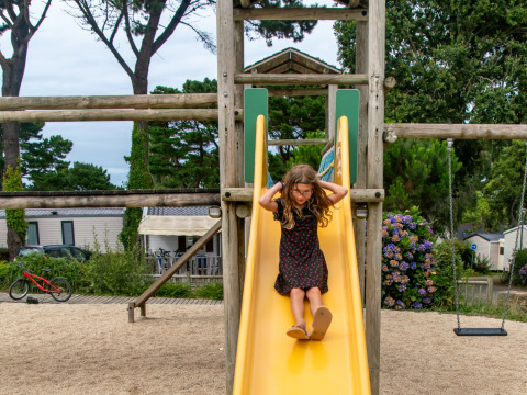 Ein Mädchen rutscht eine gelbe Rutsche auf dem Spielplatz im Flower Camping Port de la Chaîne in Bretagne hinunter.