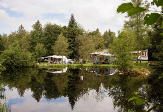 Campeggio sul lago con roulotte e tende circondate da alberi a Flower Camping La Sténiole, Grand Est, Francia.