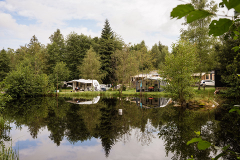 Camping au bord d’un lac avec caravanes et tentes entourés d’arbres à Flower Camping La Sténiole, Grand Est, France.