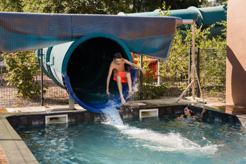 Un garçon sort d’un toboggan aquatique dans la piscine, observé par une fille, Flower Camping La Sténiole, Grand Est, France.