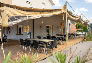 Outdoor terrace at Flower Camping La Sténiole in Grand Est, France, with tables, chairs, and canvas awning.