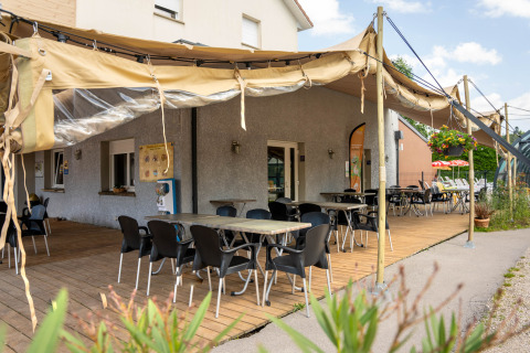 Buitenterras bij Flower Camping La Sténiole in Grand Est, Frankrijk, met tafels, stoelen en zonwering.