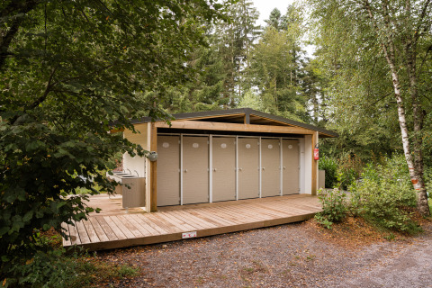 Buiten sanitairgebouw met meerdere deuren en houten terras bij Flower Camping La Sténiole, omgeven door bos.