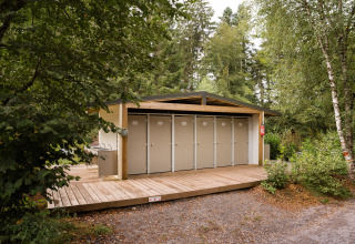 Outdoor restroom facility with multiple doors and wooden deck surrounded by forest at Flower Camping La Sténiole.