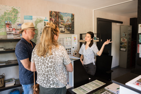 Two guests receive information from a receptionist at Flower Camping La Sténiole in Grand Est, France.