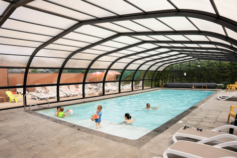 Families enjoy a covered swimming pool with lounge chairs at Flower Camping La Sténiole in Grand Est, France.