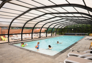 Families enjoy a covered swimming pool with lounge chairs at Flower Camping La Sténiole in Grand Est, France.