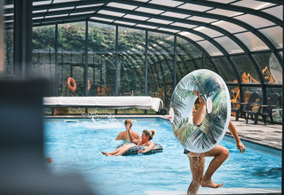 Piscine couverte à Flower Camping La Sténiole avec des vacanciers jouant et se relaxant sur des bouées gonflables.