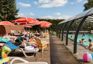 Außenpoolbereich im Flower Camping La Sténiole mit Menschen, Sonnenliegen und Sonnenschirmen im Sommer.