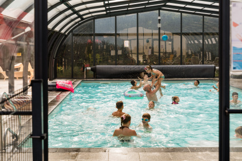 Enfants et adultes profitent ensemble d'une piscine couverte au Flower Camping La Sténiole en France.