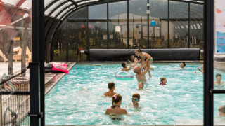 Børn og voksne leger sammen i en indendørs swimmingpool på Flower Camping La Sténiole i Frankrig.