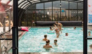 Niños y adultos se divierten juntos en una piscina cubierta en Flower Camping La Sténiole, Francia.