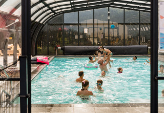 Børn og voksne leger sammen i en indendørs swimmingpool på Flower Camping La Sténiole i Frankrig.