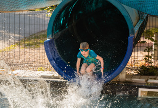 Een kind komt uit een blauwe glijbaan in het zwembad bij Flower Camping La Sténiole in Grand Est, Frankrijk.