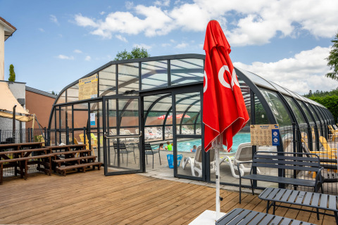 Piscina cubierta de cristal con sombrilla roja y terraza de madera en Flower Camping La Sténiole, Grand Est, Francia.