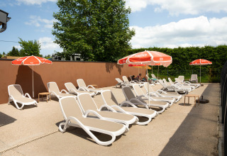 Sonnenterrasse mit Liegestühlen und Sonnenschirmen im Flower Camping La Sténiole, Grand Est, Frankreich.
