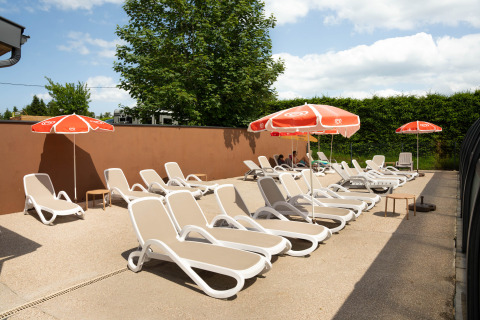 Sonnenterrasse mit Liegestühlen und Sonnenschirmen im Flower Camping La Sténiole, Grand Est, Frankreich.