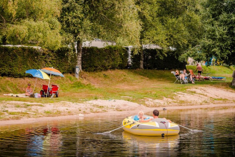 Families relaxing by a lake at Flower Camping La Sténiole, Grand Est, France, with a rowboat and umbrella.