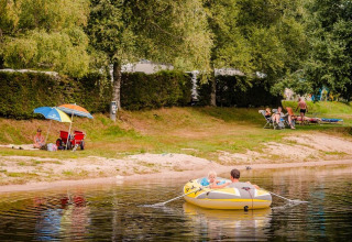 Familles profitant du lac au Flower Camping La Sténiole, Grand Est, France, avec barque et parasol coloré.
