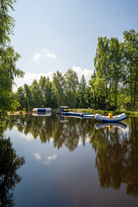 Opblaasbare speeltuigen op vijver bij Flower Camping La Sténiole, Grand Est, Frankrijk, omgeven door bomen.