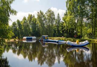 Giochi gonfiabili acquatici su uno stagno circondato da alberi a Flower Camping La Sténiole, Grand Est, Francia.