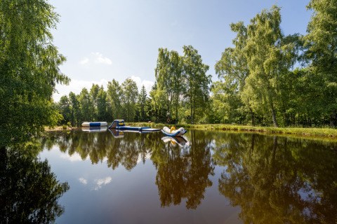 Lago tranquilo con obstáculos inflables rodeado de árboles en Flower Camping La Sténiole, Grand Est, Francia.