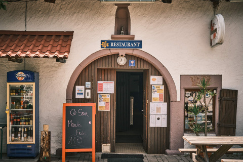 Photo extérieure d’une entrée de restaurant avec enseigne, frigo à boissons et ardoise à Flower Camping La Sténiole.