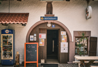 Outdoor photo of a restaurant entrance with a sign, drinks fridge and chalkboard at Flower Camping La Sténiole.