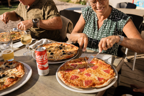 Deux personnes dégustent des pizzas et des boissons en plein air à Flower Camping La Sténiole, Grand Est, France.