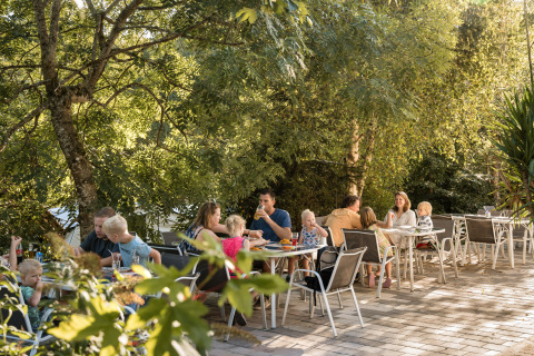 Gezinnen eten buiten onder bomen bij Flower Camping La Sténiole, een vakantiedomein in Grand Est, Frankrijk.