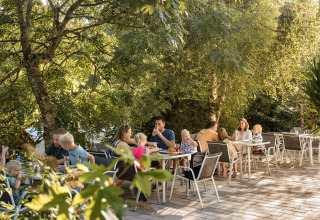 Des familles dînent en plein air sous les arbres au Flower Camping La Sténiole, Grand Est, France.