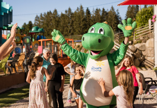Børn har det sjovt med en grøn dinosaur-maskot ved Flower Camping La Sténiole i Grand Est, Frankrig.