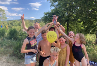 Groep blije kinderen bij Flower Camping La Sténiole met een gele ballon en een kartonnen figuur buiten.