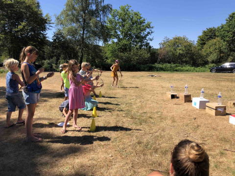Børn leger bueskydning udendørs på en solrig dag i Flower Camping La Sténiole, Grand Est, Frankrig.