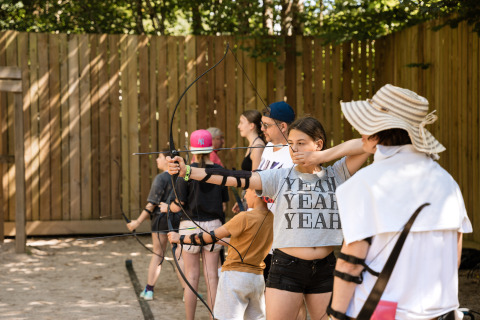 Bambini e adulti praticano il tiro con l'arco all'aperto al Flower Camping La Sténiole in Grand Est, Francia.