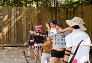 Kinder und Erwachsene üben Bogenschießen im Freien im Flower Camping La Sténiole in Grand Est, Frankreich.