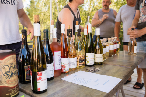 Buiten wijnproeverij bij Flower Camping La Sténiole, Grand Est, Frankrijk, met flessen op een houten tafel.
