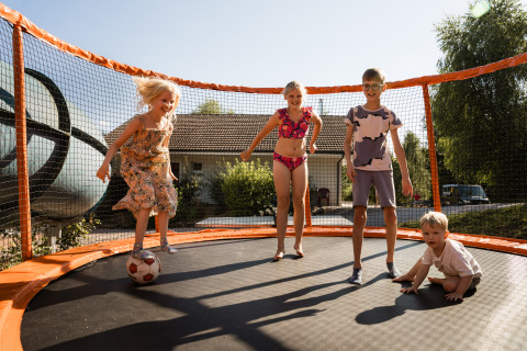 Children playing on a trampoline in the sunshine at Flower Camping La Sténiole holiday park in Grand Est, France.