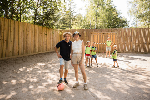 Two adults and several children enjoy playing soccer together outside at Flower Camping La Sténiole, France.