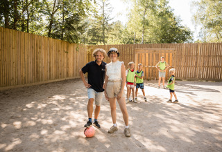 Zwei Erwachsene und mehrere Kinder spielen gemeinsam Fußball auf einem Sandfeld im Flower Camping La Sténiole.