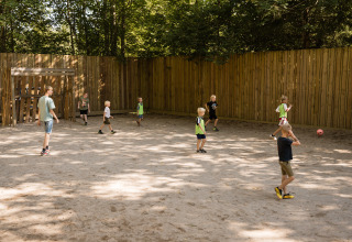 Kinderen spelen voetbal op een stoffig veld met houten omheining bij Flower Camping La Sténiole in Grand Est, Frankrijk.