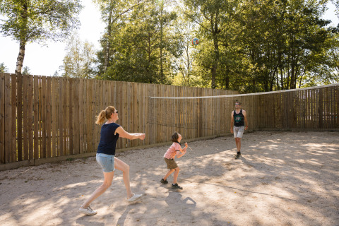 Familie spielt Volleyball auf einem Sandplatz mit Holzzaun im Flower Camping La Sténiole, Grand Est, Frankreich.