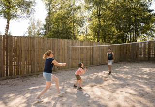 Famiglia gioca a pallavolo su un campo sabbioso recintato in legno a Flower Camping La Sténiole, Grand Est, Francia.
