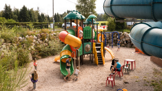 Børn leger på en farverig legeplads med rutschebaner og klatrestativer i Flower Camping La Sténiole, Grand Est.